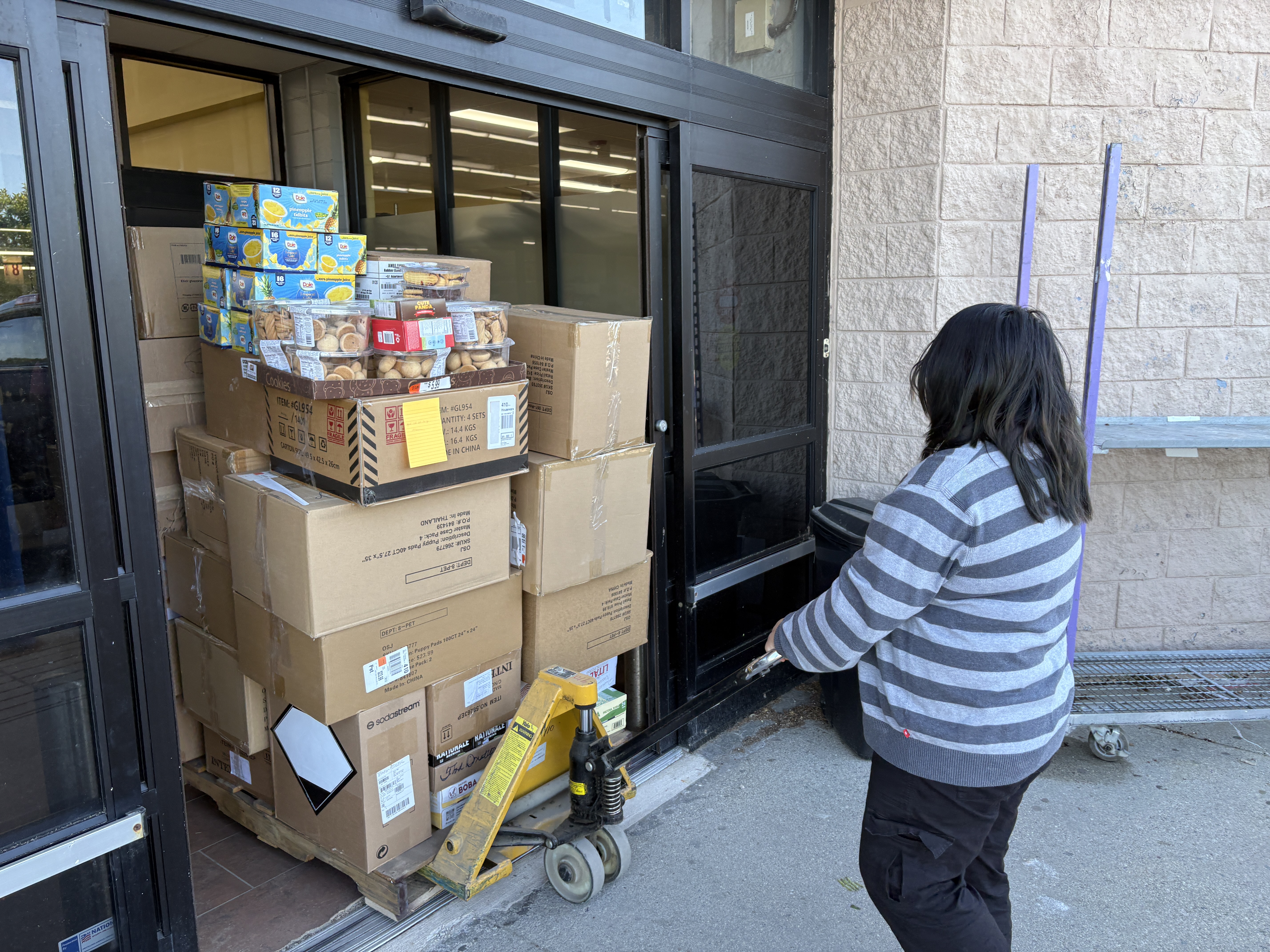 Boxes of donated food and supplies stacked on a pallet jack at an Ocean State Job Lot doorway